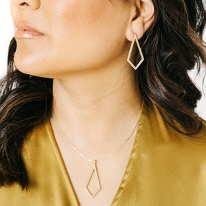 Woman wearing minimalist kite shaped earrings in yellow bronze