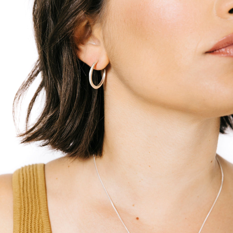 Woman wearing minimalist crescent hoop earrings in silver
